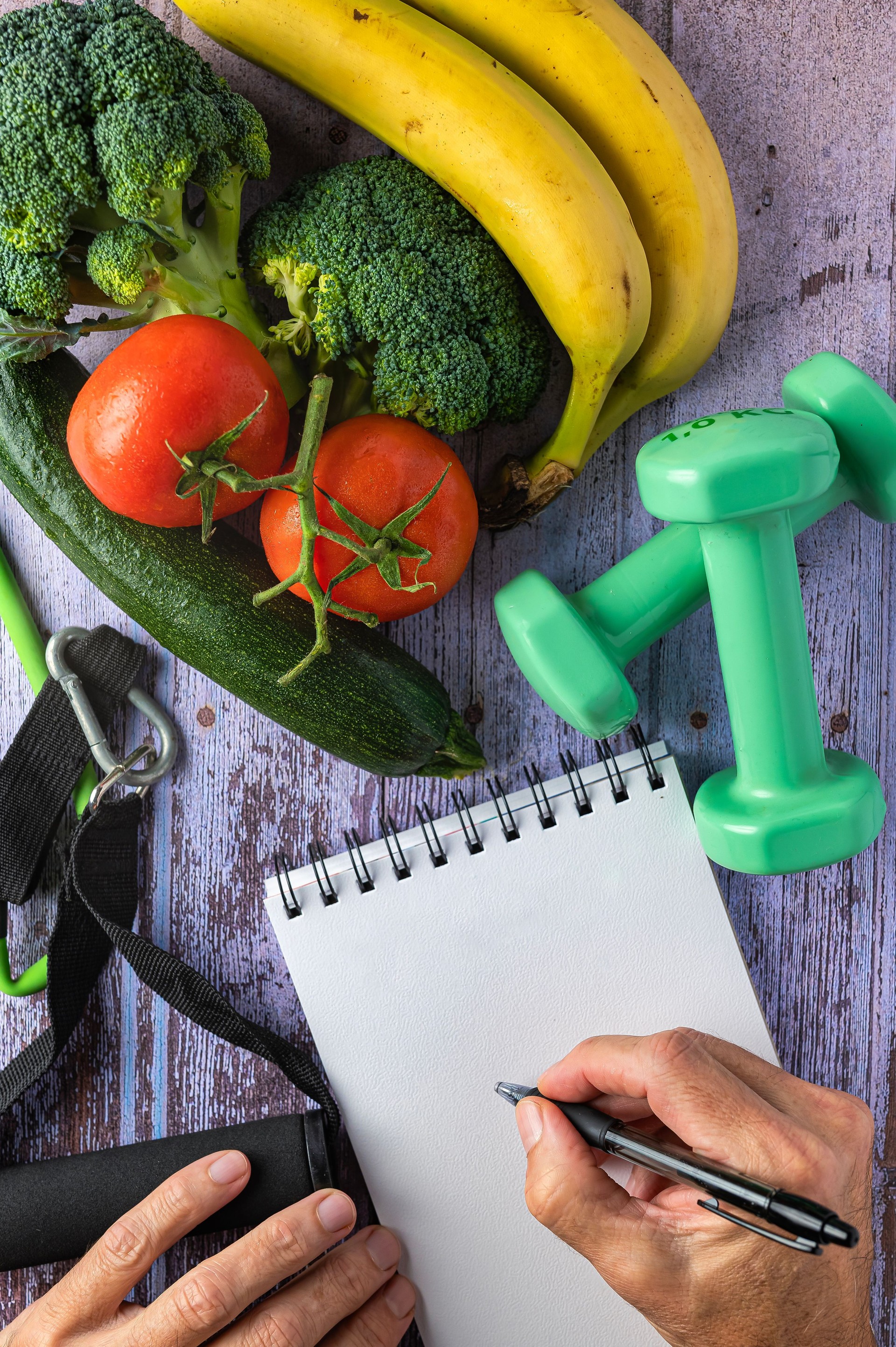 Fresh vegetables, two hands and a notepad, dumbbells and elastic, healthy lifestyle concept
